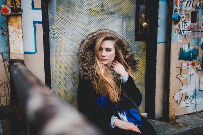 Woman with fur-hooded coat sitting by graffiti-covered door