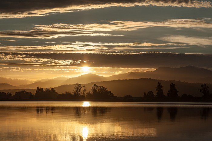 Sunset over mountains and lake with sun rays