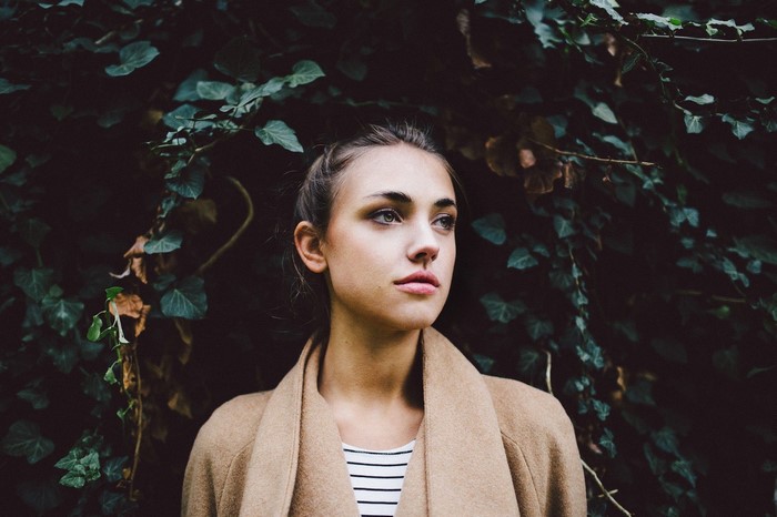 Woman in a tan coat standing in front of ivy