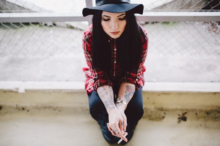 Woman in plaid shirt and hat holding a cigarette