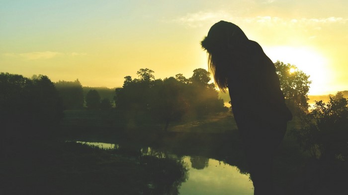 Silhouette of a woman by a lake at sunrise