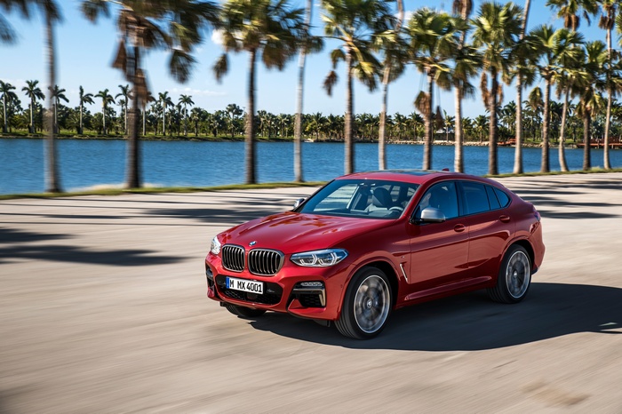 Red BMW X4 driving by a lake with palm trees