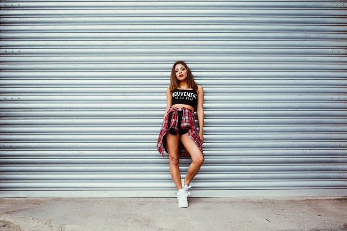 Woman in crop top and plaid shirt standing against metal wall
