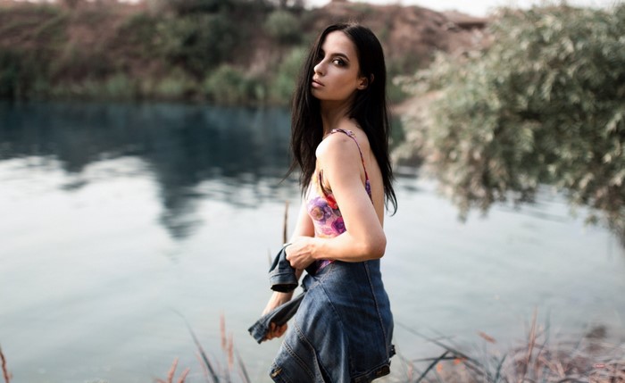 Woman in floral dress and denim jacket by a lake