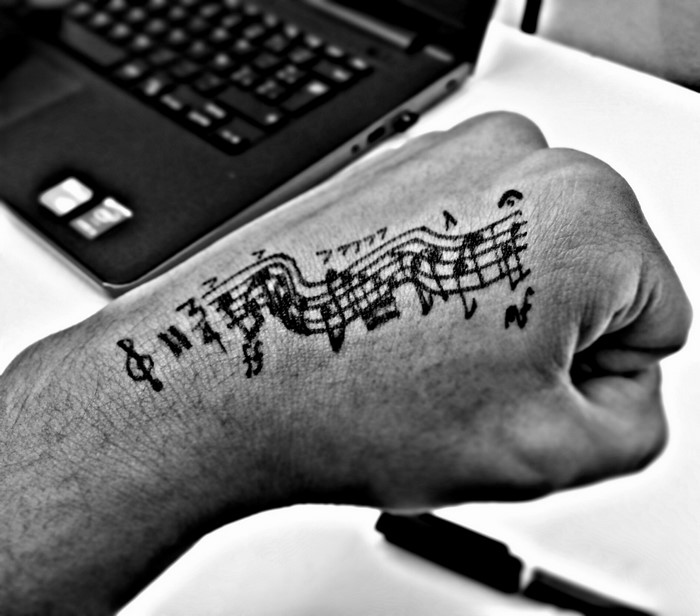 Hand with musical notes tattoo and laptop