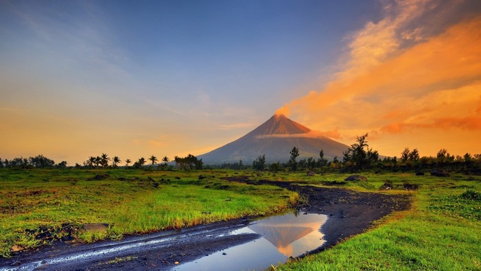 Volcano erupting at sunset with reflection in water