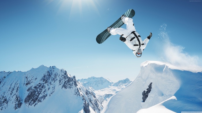 Snowboarder performing a flip over a snowy mountain jump
