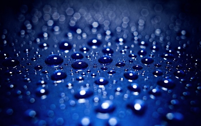 Close-up of water drops on a blue surface with bokeh