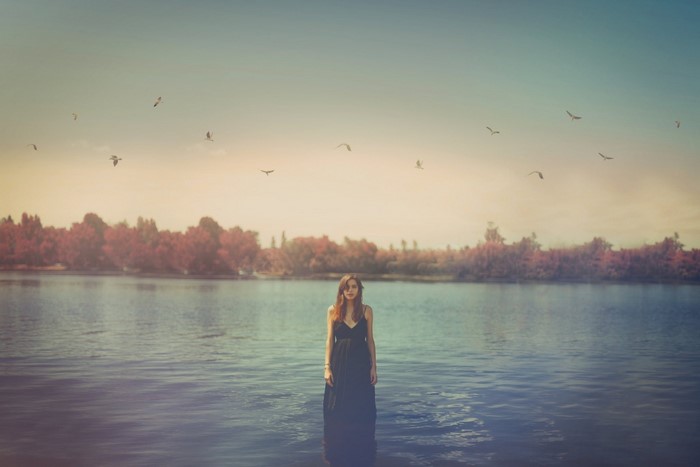 Woman in black dress standing in lake with birds flying