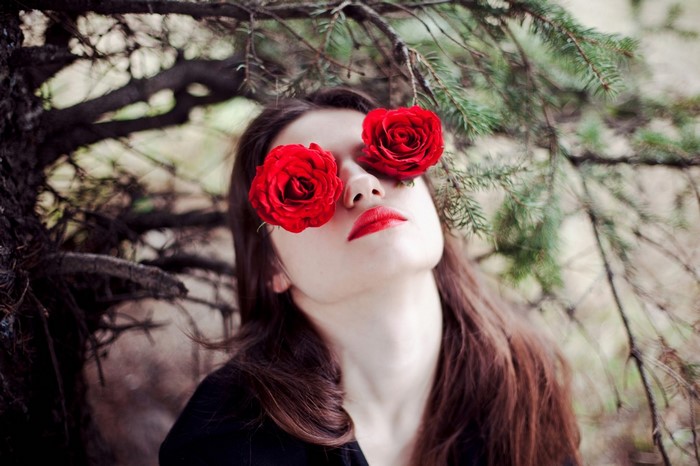 Woman with red roses over her eyes in a forest