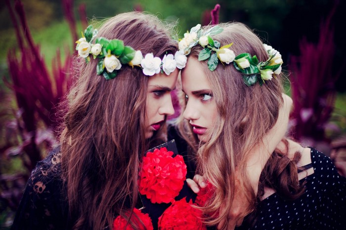 Two young women wearing flower crowns and holding red flowers
