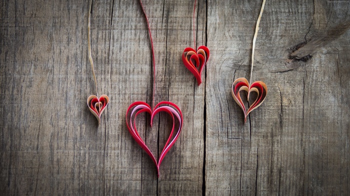 Four paper hearts hanging on strings on a wooden surface
