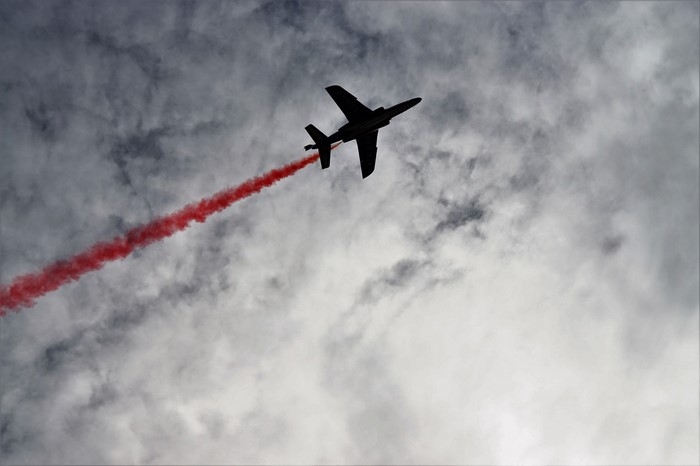 Silhouette of a jet aircraft performing aerobatics with red smoke