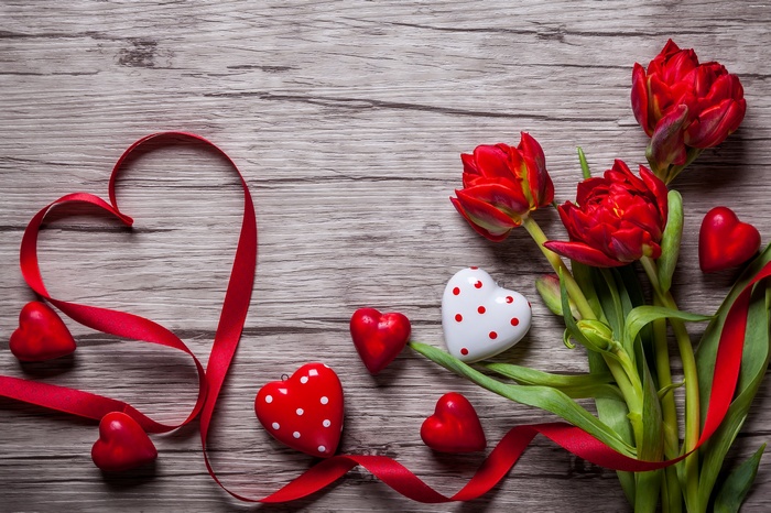 Red tulips and hearts with ribbon on wooden background