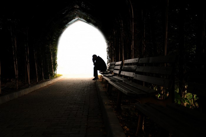 Man sitting on a bench in a dark tunnel with light ahead