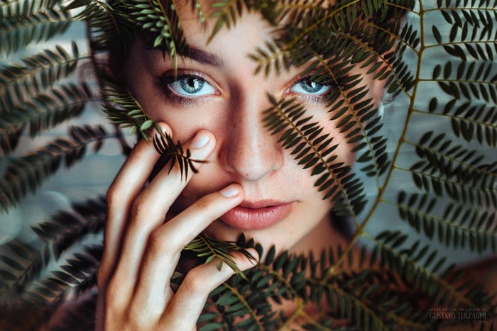Woman with blue eyes behind green fern leaves