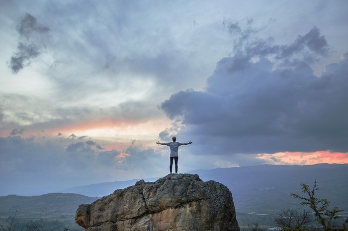 Man with arms outstretched on a rock at sunset