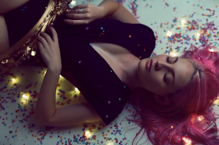 Woman with pink hair lying down with confetti and lights