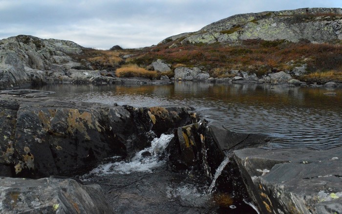 Rocky stream flowing into a calm lake with hills