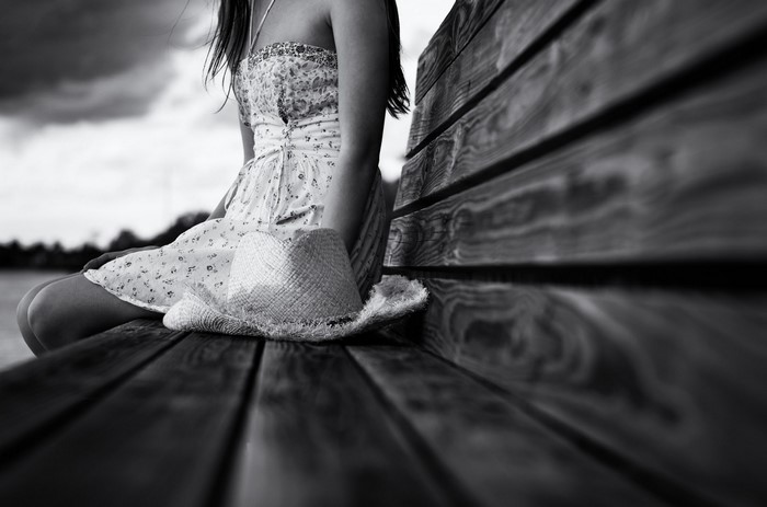 Woman in dress with hat sitting on a wooden bench