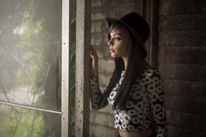 Woman in a floral top and hat looking out a window