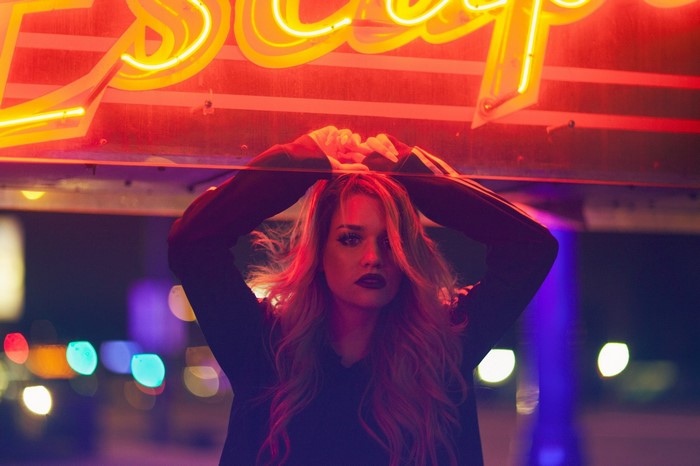 Woman with hands on head under neon sign