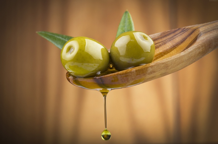 Green olives with olive oil on a wooden spoon