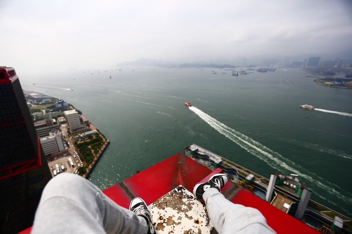 Person sitting on edge of skyscraper overlooking a bay with boats