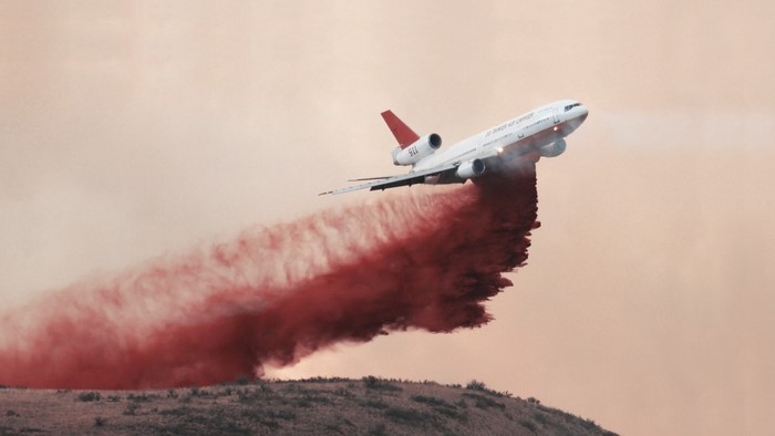 Airplane dropping red retardant on a hillside