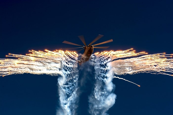 Helicopter deploying flares against a dark blue sky
