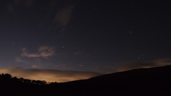Night sky with stars and clouds over a silhouetted hill