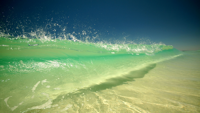 Green wave crashing under a clear blue sky