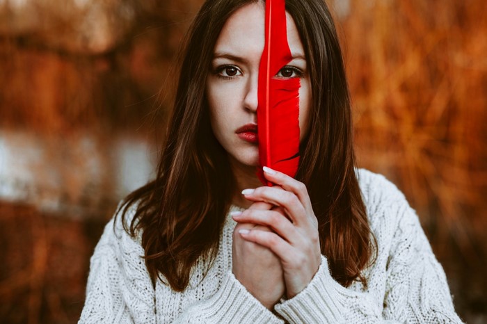 Woman holding a red feather in front of her face