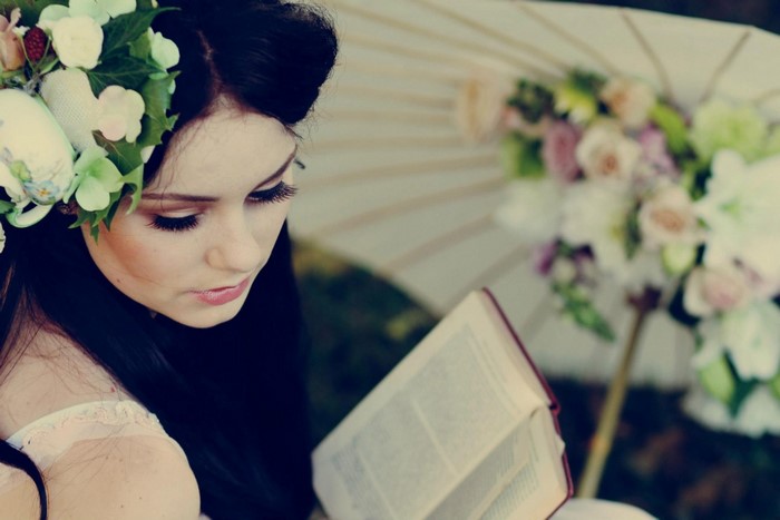 Woman with flowers in hair reading a book near an umbrella