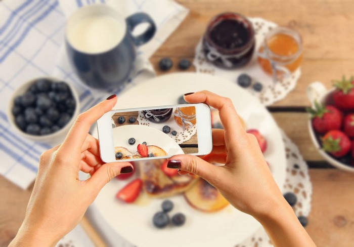Woman taking a photo of a breakfast with pancakes and berries