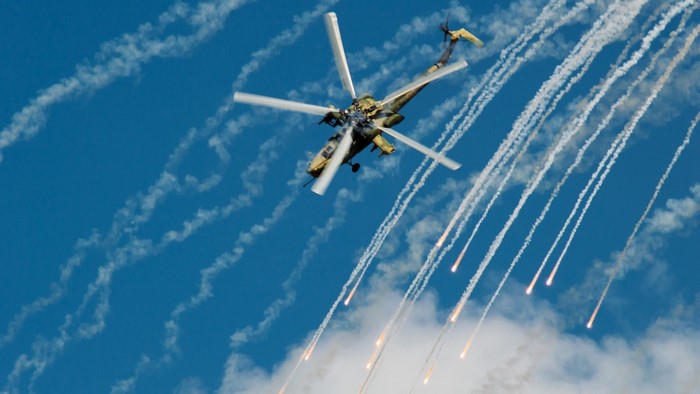 Military helicopter firing flares against a blue sky