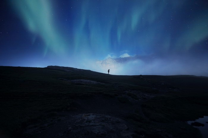 Person watching Aurora Borealis over mountains at night