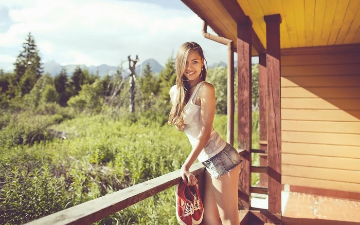 Woman in jean shorts holding red shoes on a porch