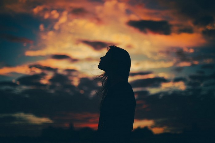 Silhouette of a woman against a dramatic sunset sky
