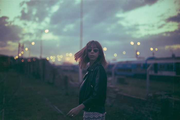 Woman in leather jacket at dusk with train tracks