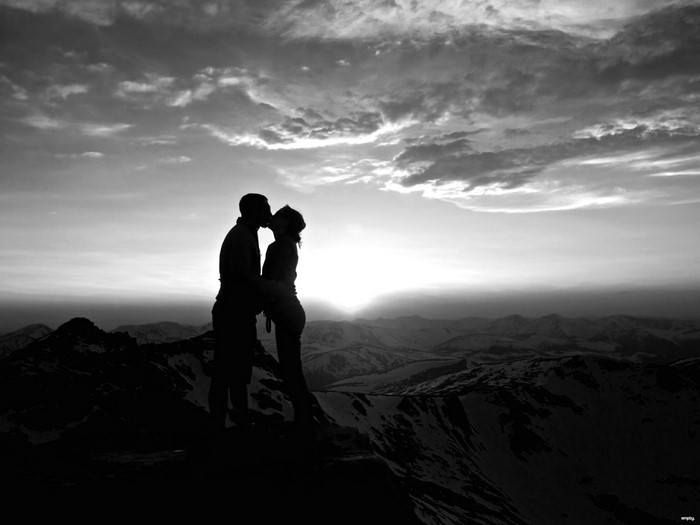 Couple kissing on mountain peak at sunset silhouette