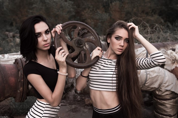 Two women posing with a large valve wheel