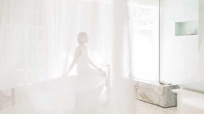 Woman in white dress sitting by a bathtub in a bright room