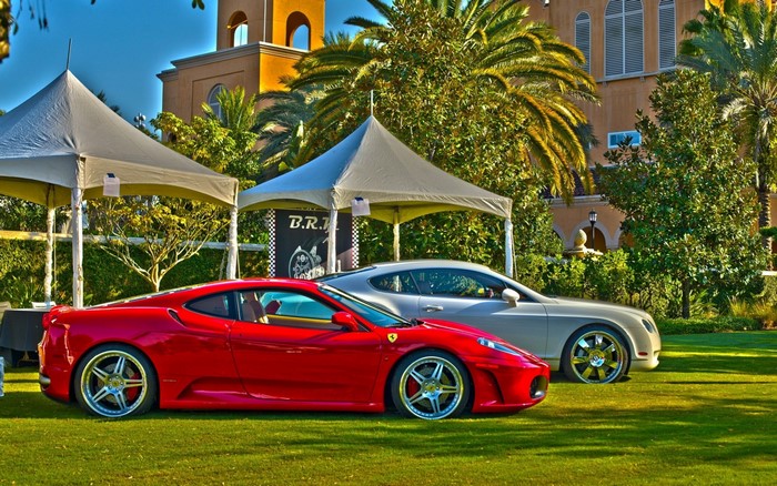Red Ferrari and Silver Bentley parked on grass