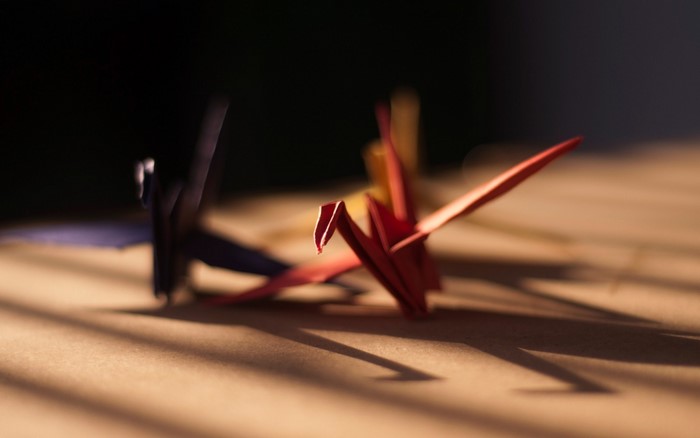 Red and blue origami cranes casting shadows