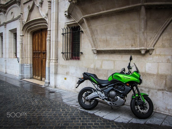 Green Kawasaki Versys motorcycle parked on cobblestone street