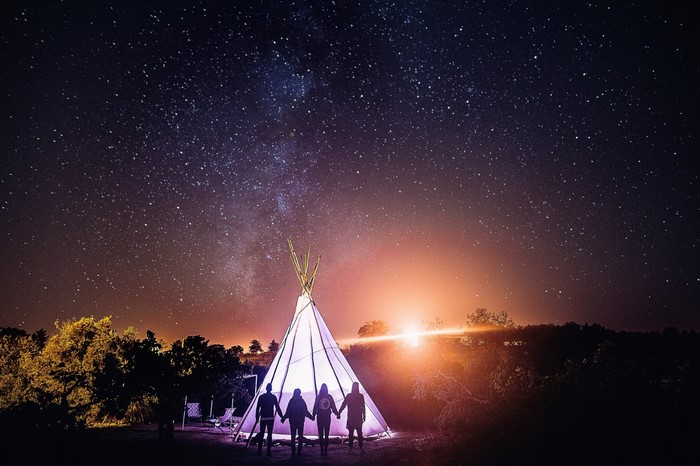 People holding hands in front of a lit tent under a starry night sky