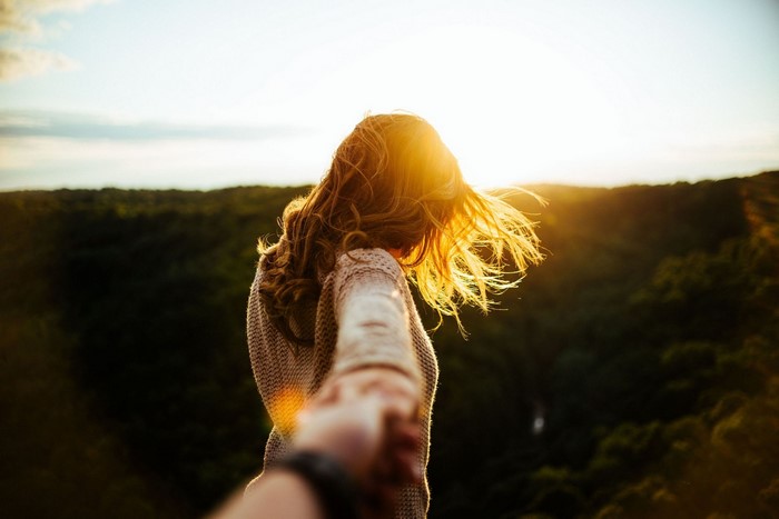 Woman holding hand at sunset over forest