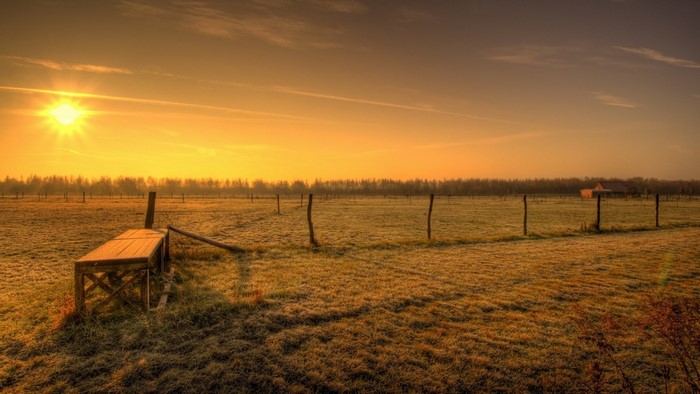 Sunrise over a frosty rural field with a wooden structure