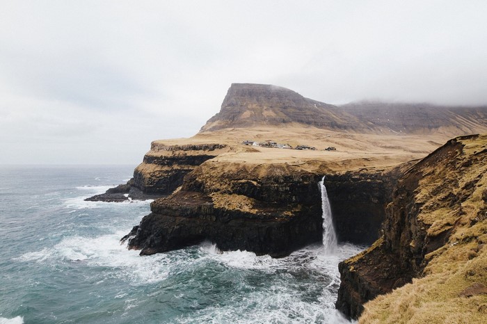Waterfall cascading from cliffs into the sea with a village on top